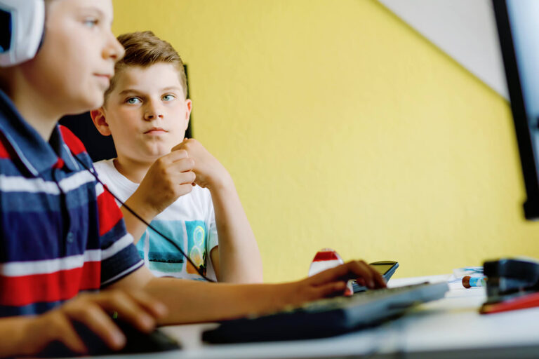 2 gutter sitter sammen foran en datamaskin i et klasserom