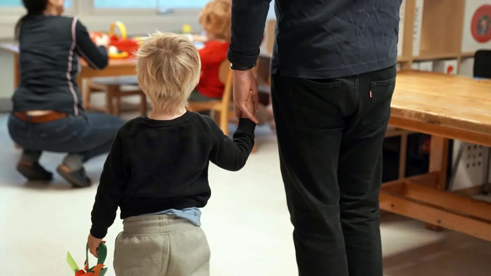 en pappa leier sin lille sonn i barnehagen rygg mot kamera