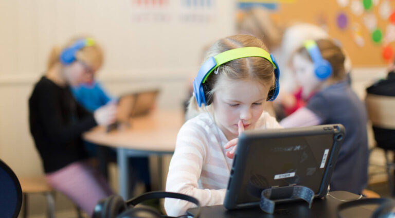 Jente med hodetelefoner og nettbrett i et klasserom