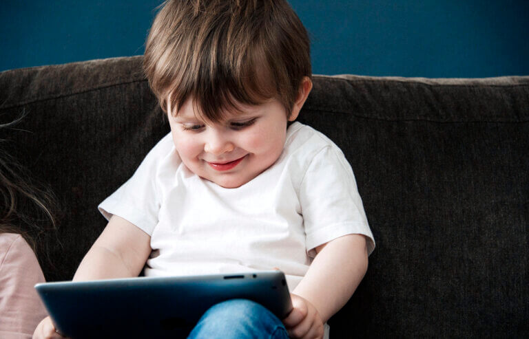 Liten gutt som sitter i en sofa med en iPad