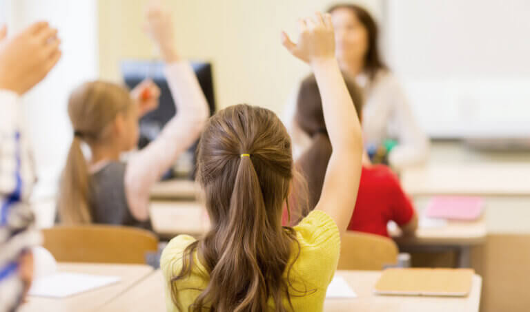 Liten jente som sitter i et klasserom og rekker opp hånden.