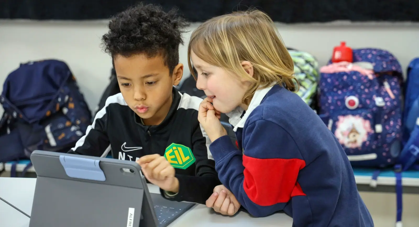 StøDig – Hva er god bruk av læringsteknologi i lese-, skrive- og språkopplæringen? to engasjerte barn sitter i klasserom foran en ipad