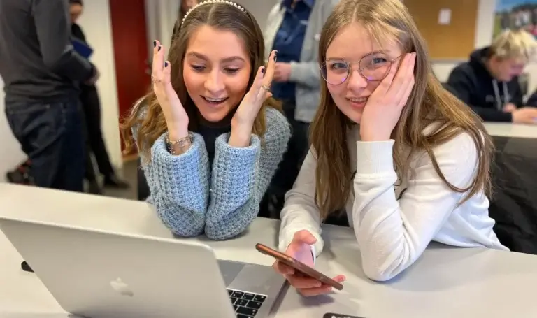 to-glade-jenter-i-klasserom-foran-berbar-pc-og-en-mobiltelefon
